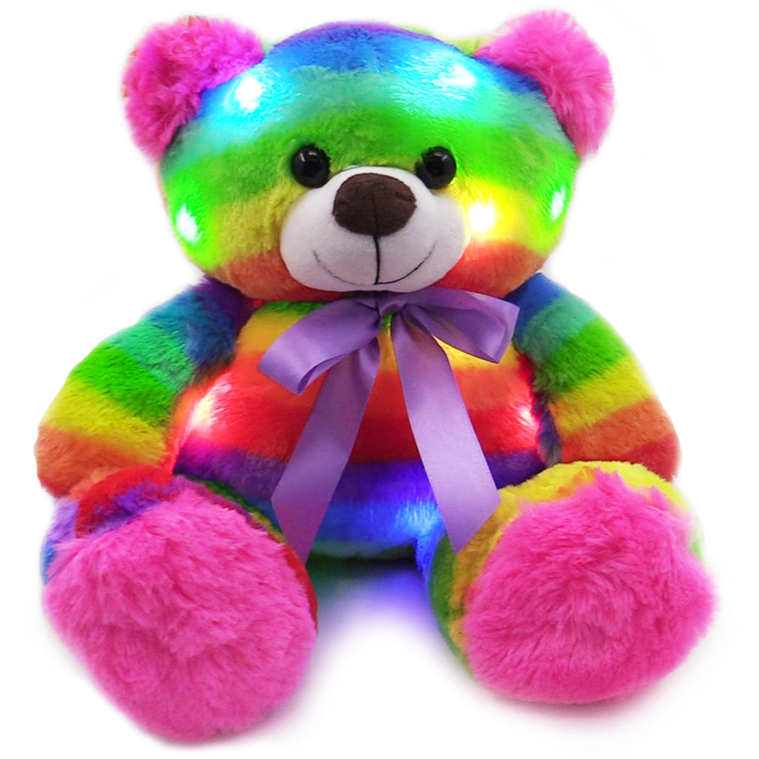 Rainbow teddy bear glow plush with pink ears and purple ribbon on white background.