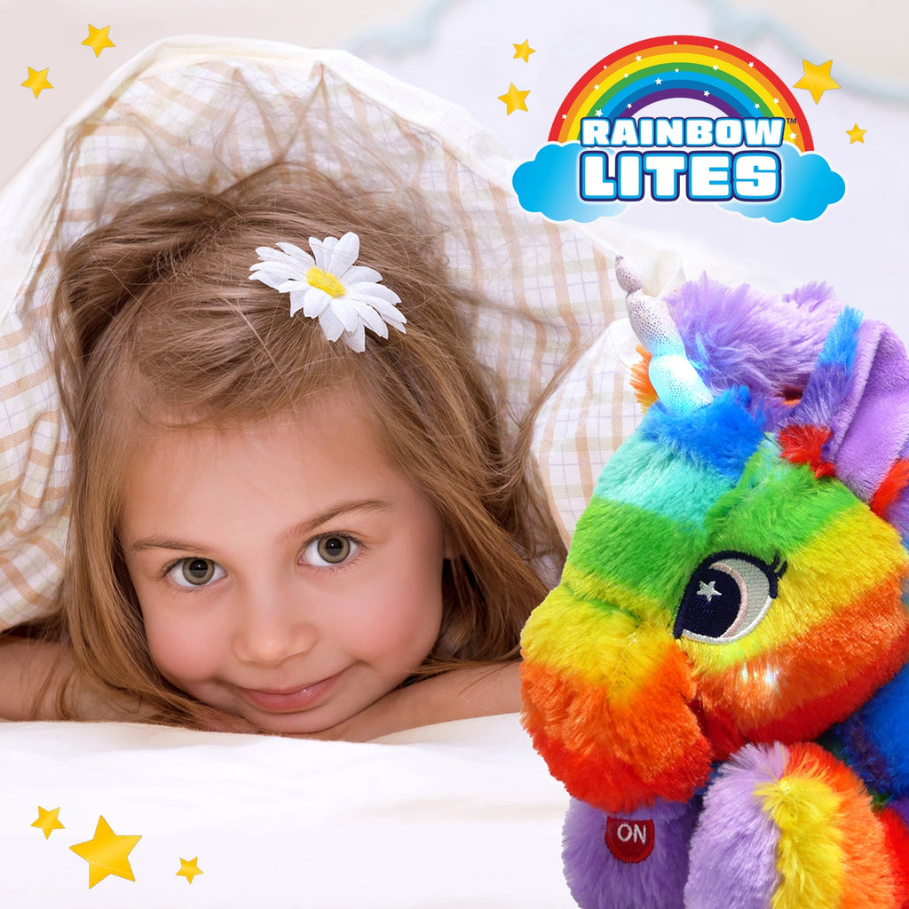 Child peeking from under blankets beside the glowing rainbow unicorn plush night light.
