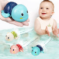 Blue wind-up turtle held in a hand beside a baby in the bath with three turtles swimming.