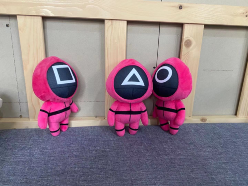 Three masked pink character plush toys seated together